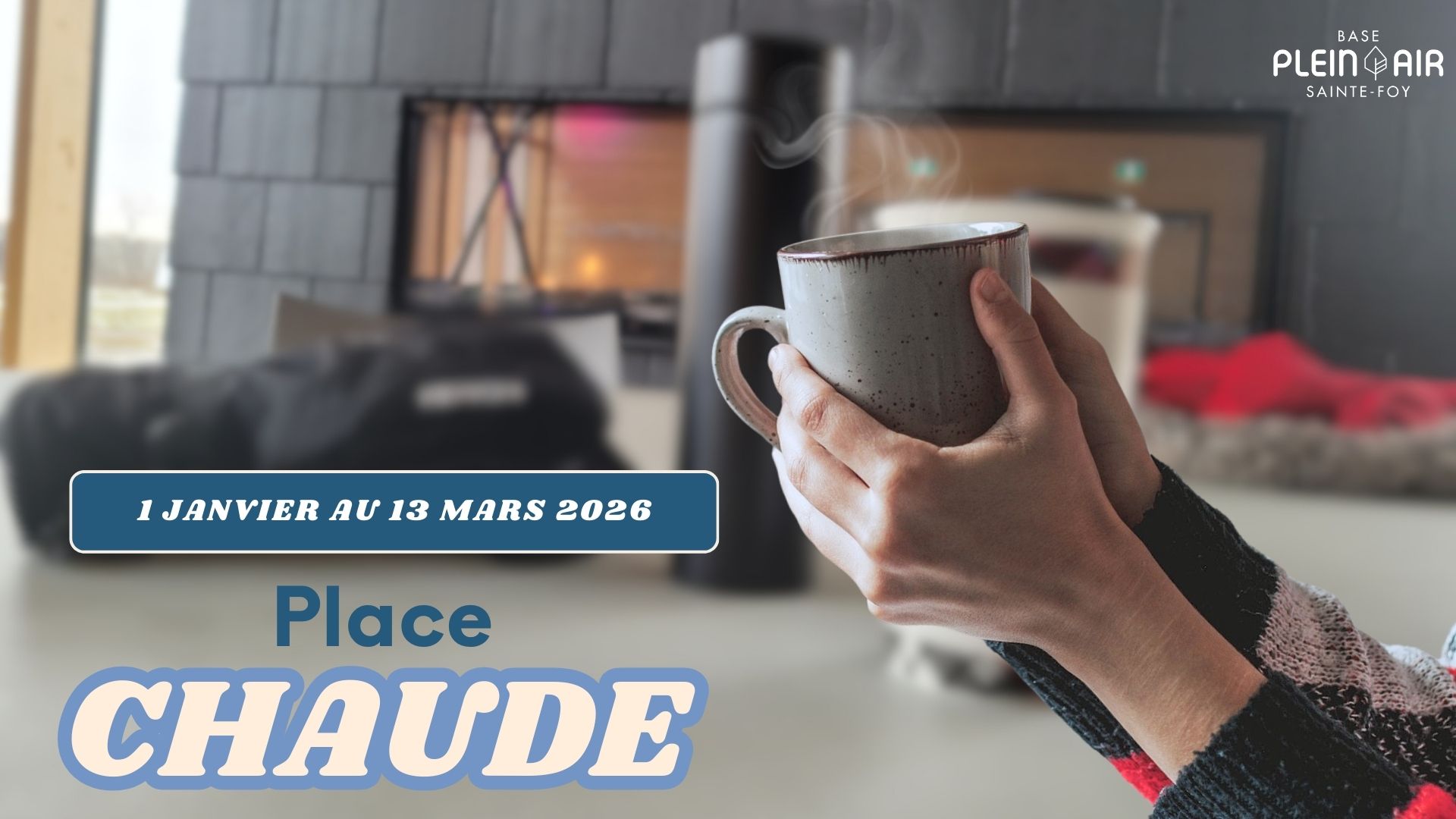 Place chaude pour l'hiver Salle multifonctionnelle en arrière plan, avec cheminé ouvert. Au premier plan une tasse de boisson chaude tenue par deux mains.